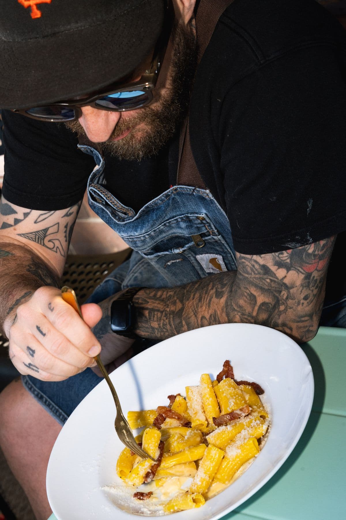 Tätowierte Hände, Jeansjacke, ein Teller Rigatoni Carbonara