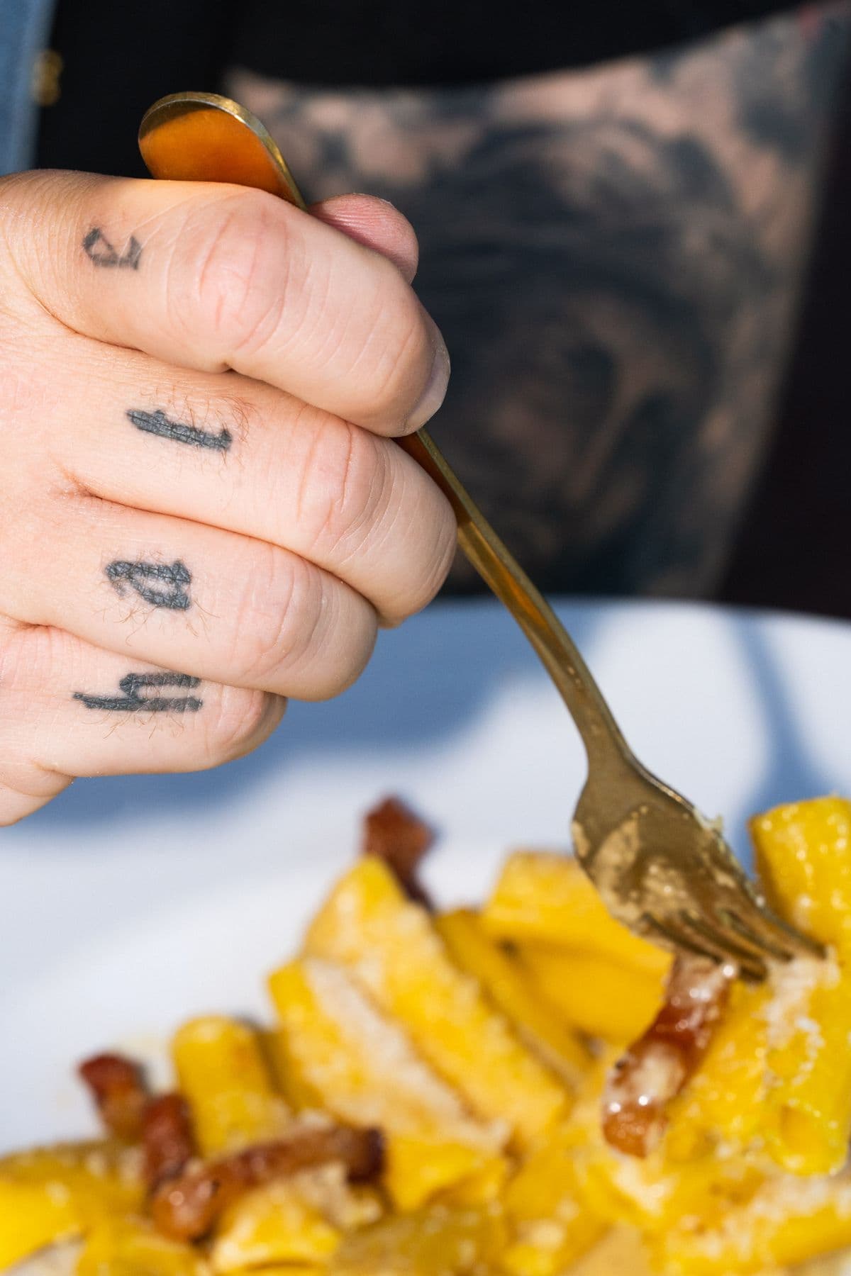 Gabel in der Carbonara, auf den Fingern tätowierte Buchstaben