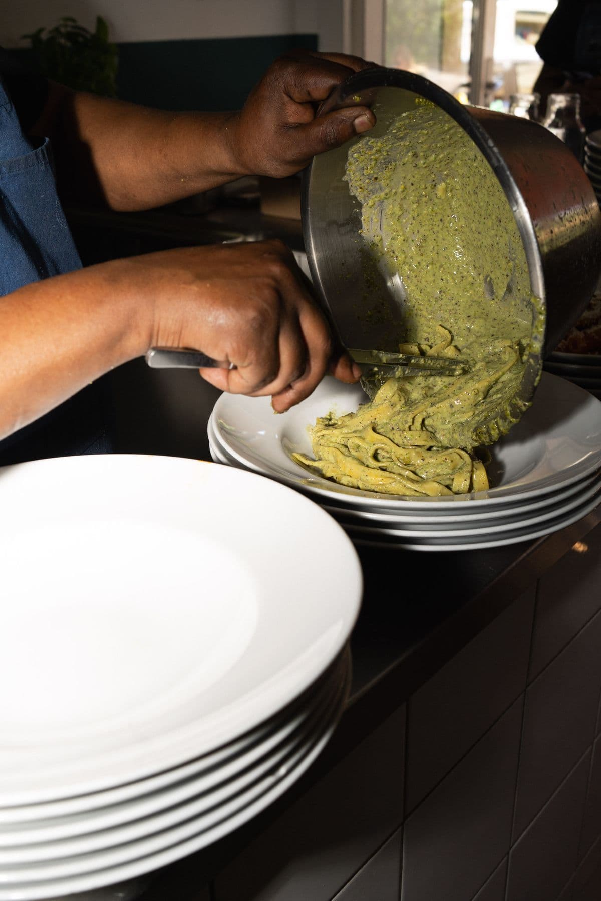 Pesto-Pasta wird aus der Pfanne auf den Teller gegeben