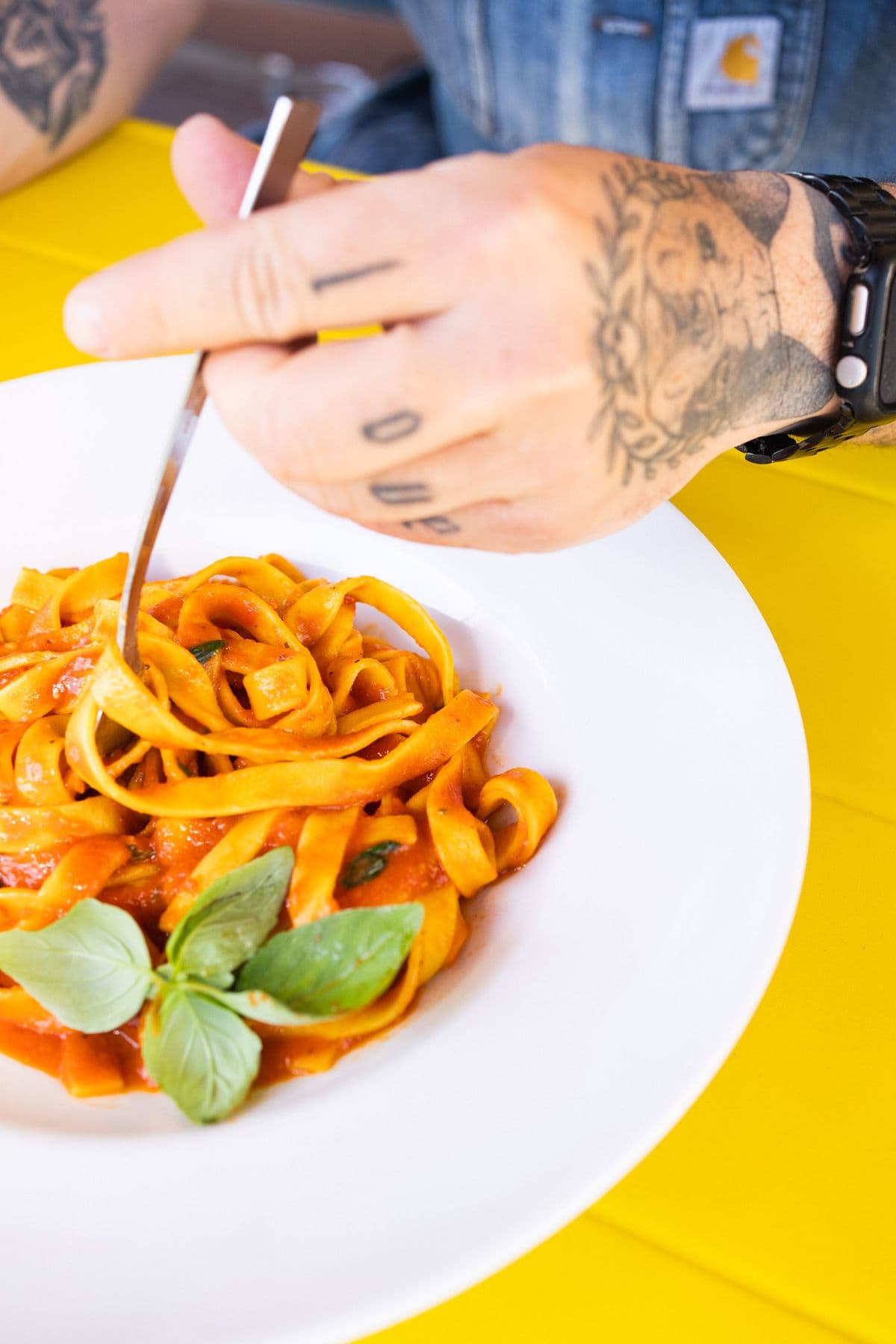 Tätowierte Hand dreht Tagliatelle al pomodoro auf die Gabel