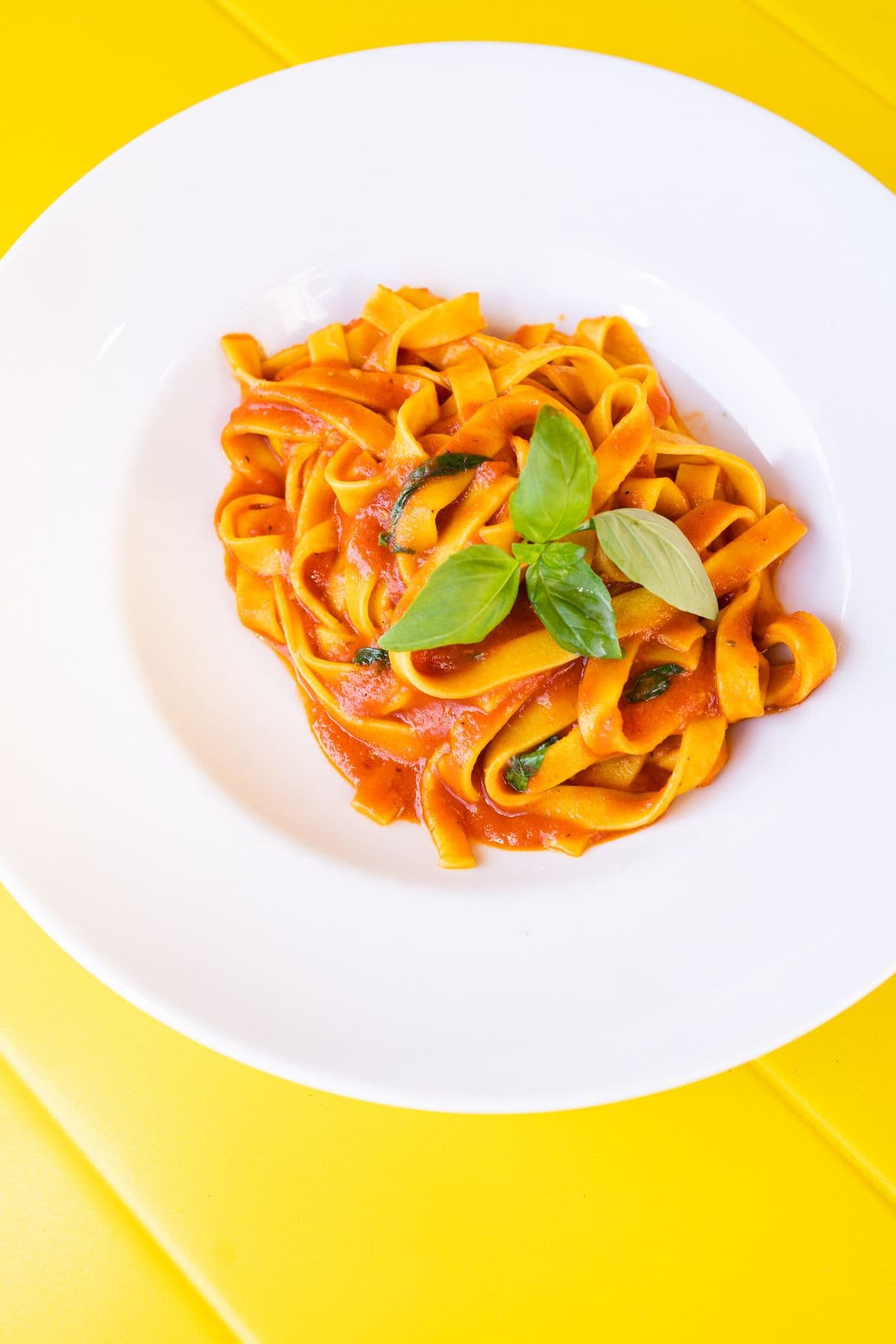 Tagliatelle al pomodoro mit Basilikum auf dem gelben Tisch, von oben