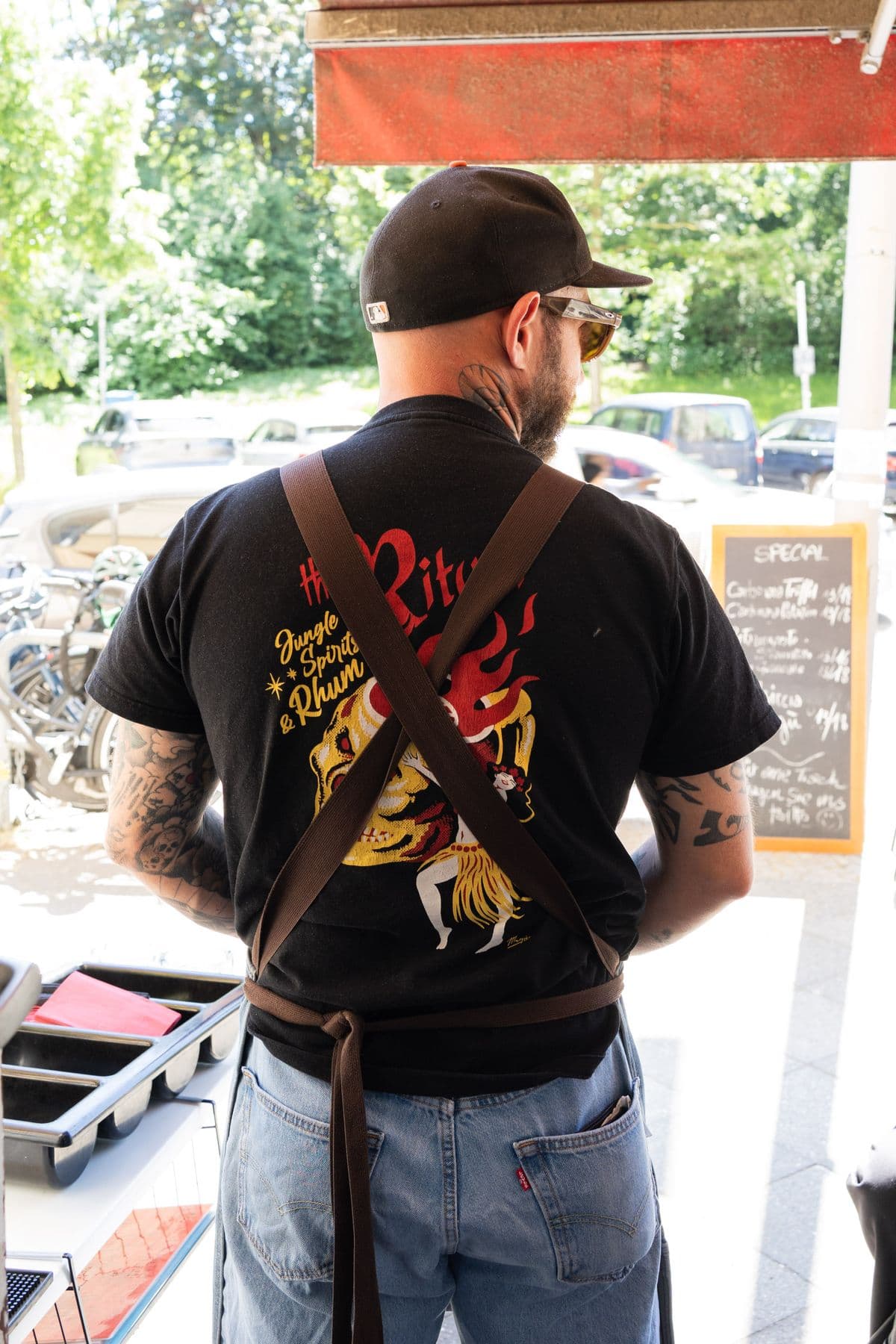 Alessandro von hinten: Shirt mit Tattoo-Print, Lederschürze, Blick auf die Straße