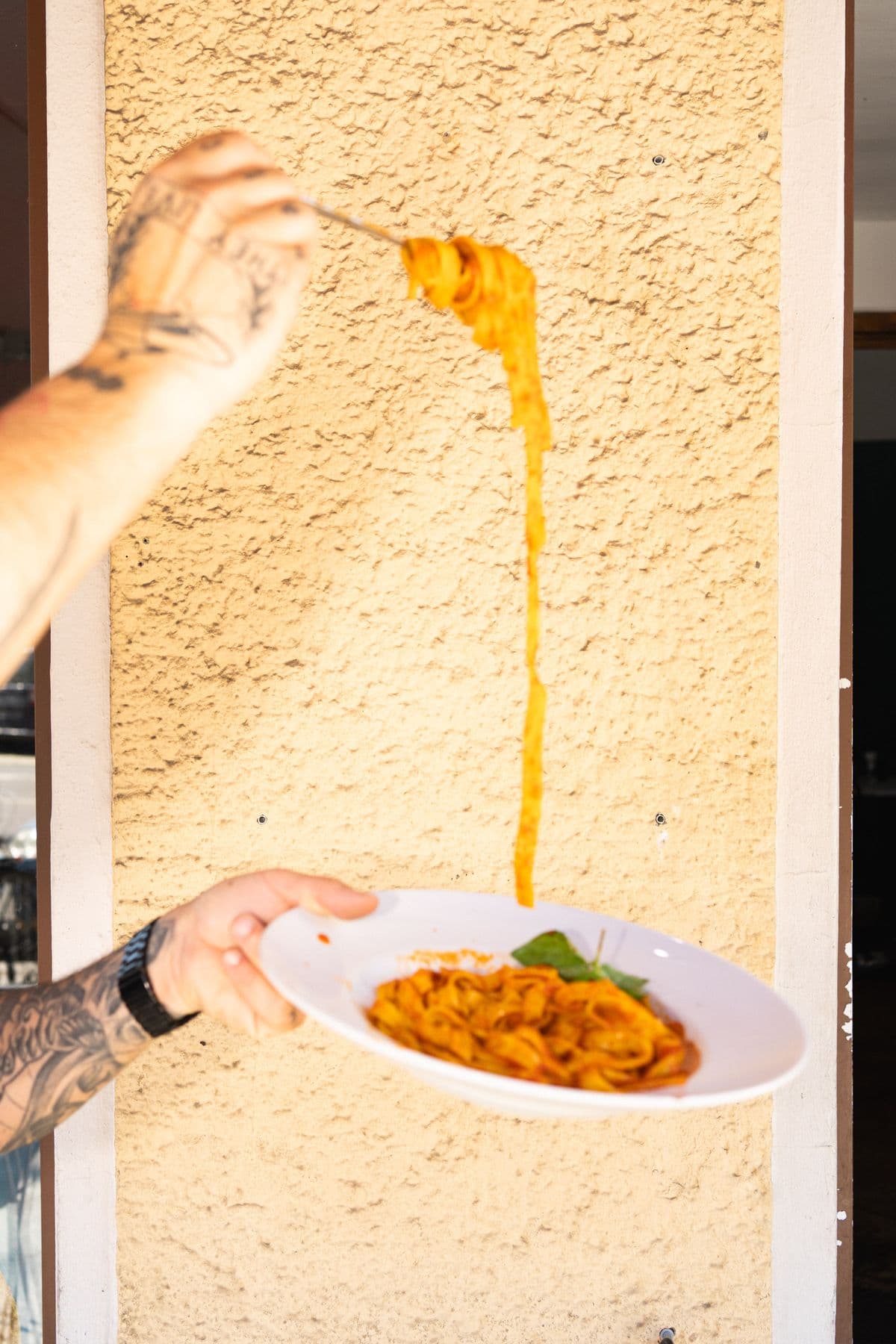 Tagliatelle mit Tomatensoße hängen hoch von der Gabel, vor der ockerfarbenen Wand