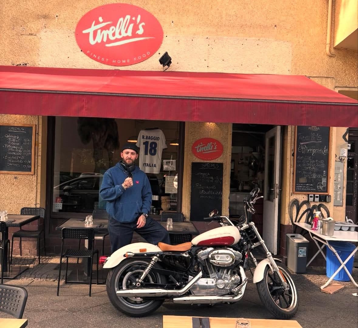 Vor Tirelli's: Harley-Davidson unter der roten Markise, im Fenster hängt das Trikot R. Baggio 18